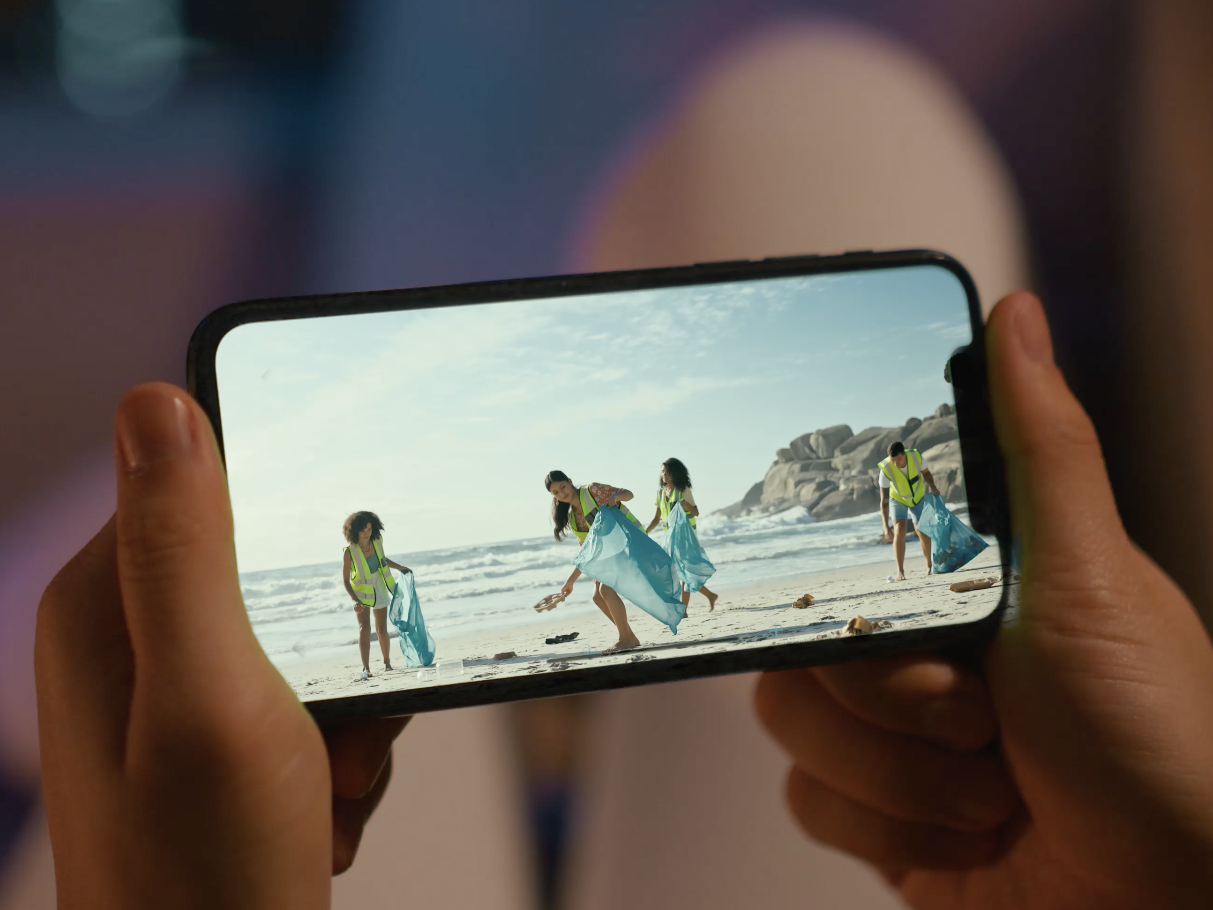 Person holding phone that shows imagery of a beach cleanup