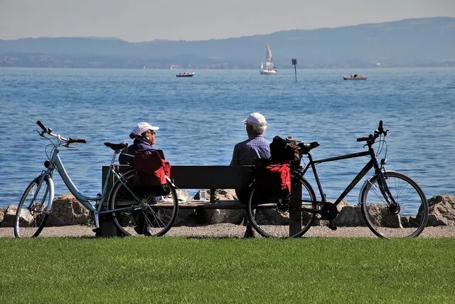 Two adults sitting on a bench looking out at water 