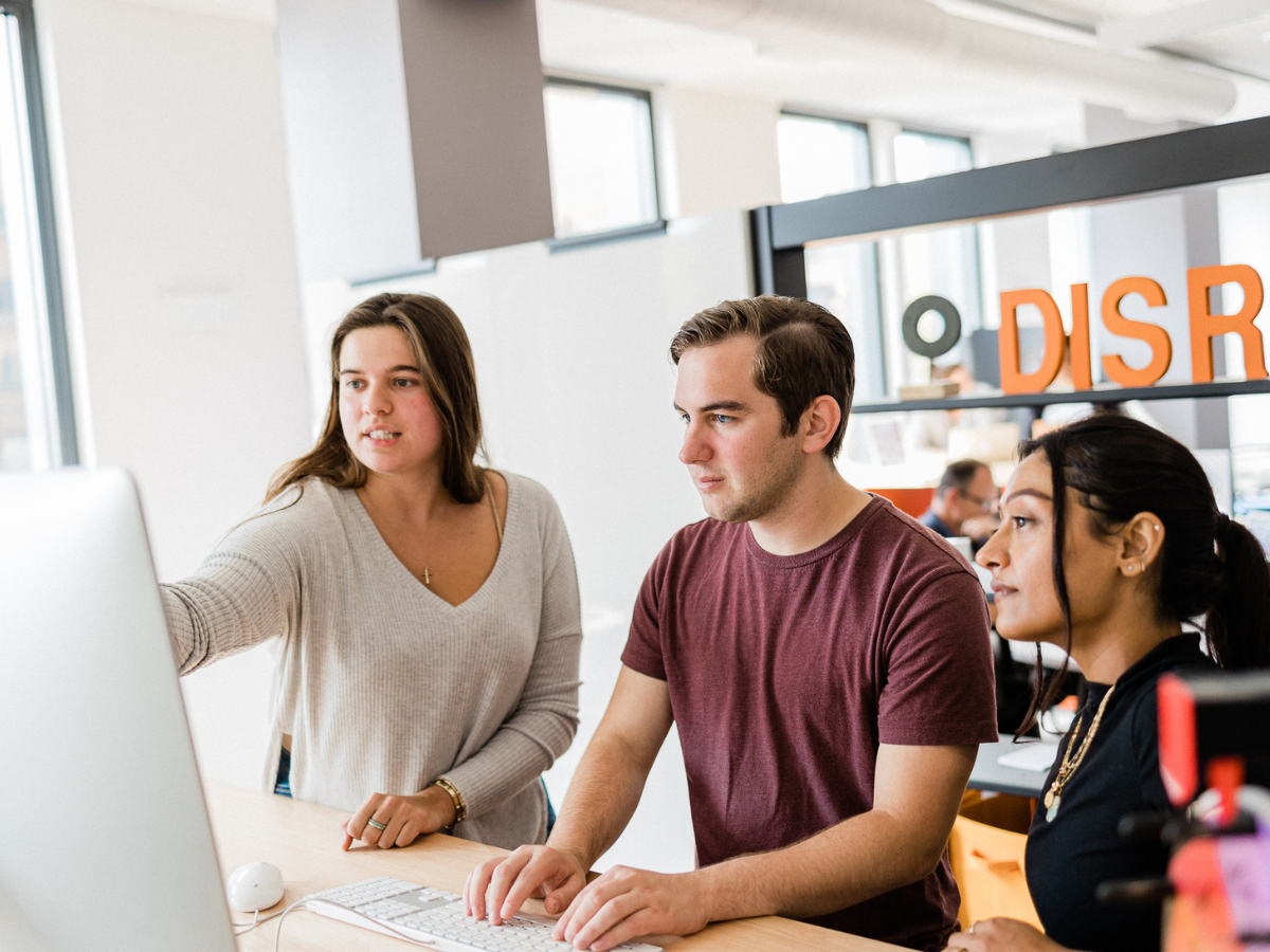 Three individuals collaborating around a computer screen