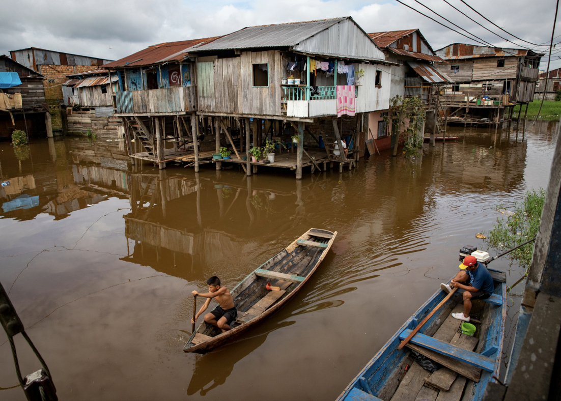 A person rowing a boat on a river among houses on stilts. 