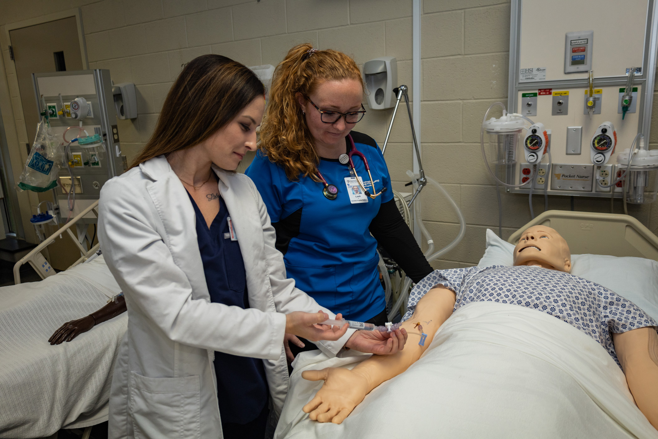 Two people work in a teaching lab on a dummy patient in a bed