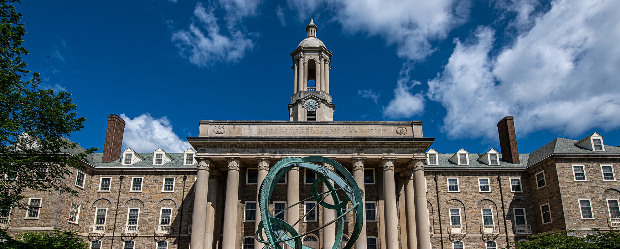 Old Main against a brilliant blue sky with the armilliary sphere in front