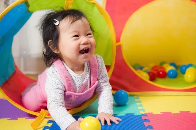 A baby crawls on the floor holding a ball