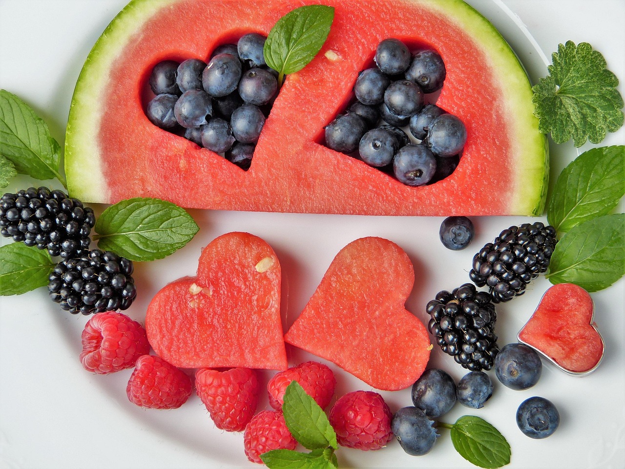 Watermelon cut out into a heart shape and blueberries, blackberries, raspberries and mint