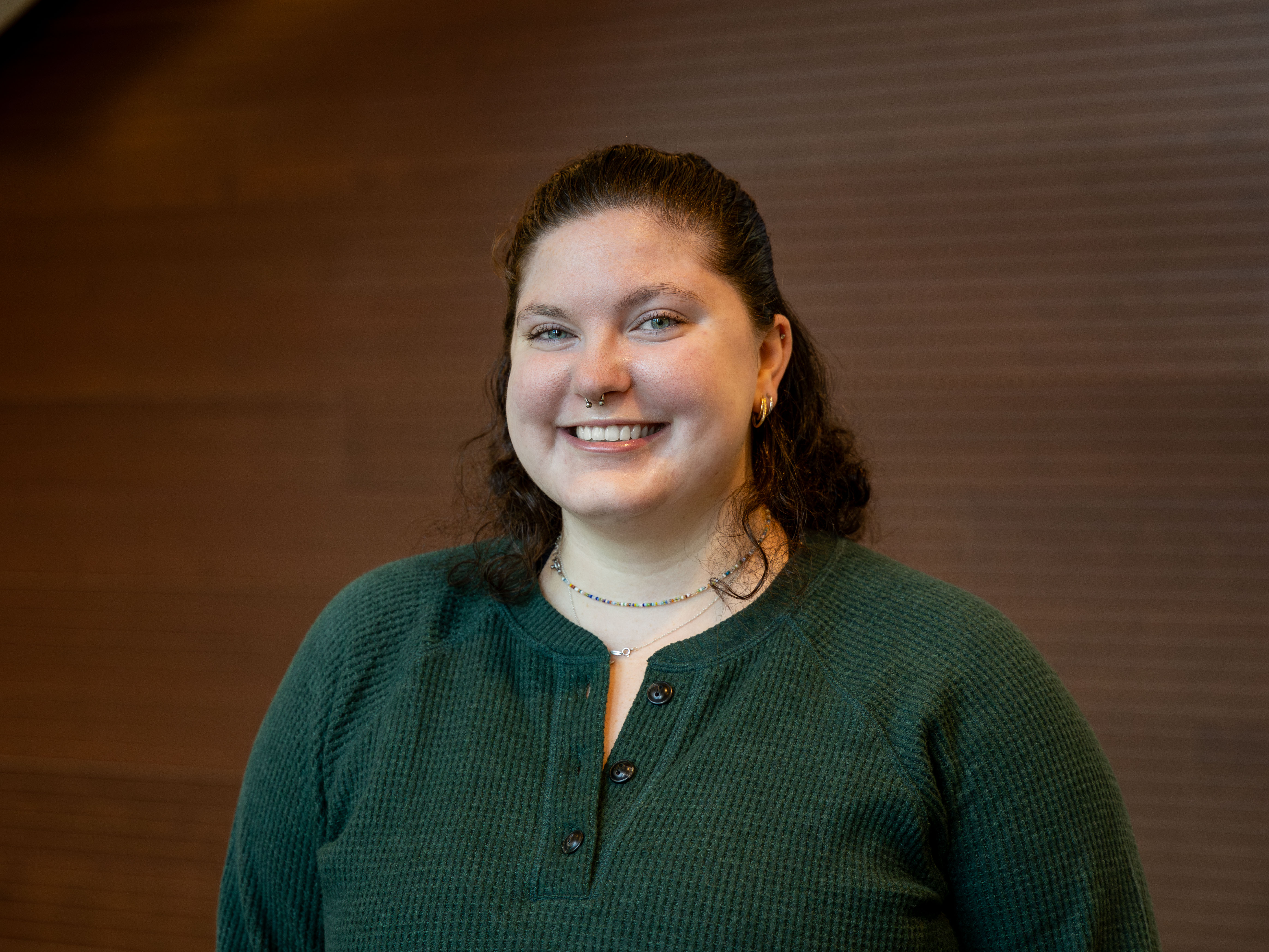 Emily Cotrufello wears a dark green shirt while smiling in front of a brown wall at Penn State University Park.