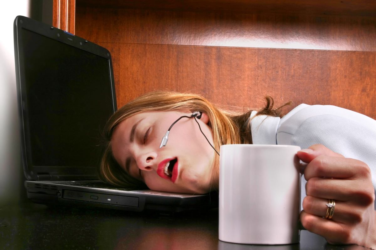 A woman sleeps on her laptop with her hand still holding her coffee.