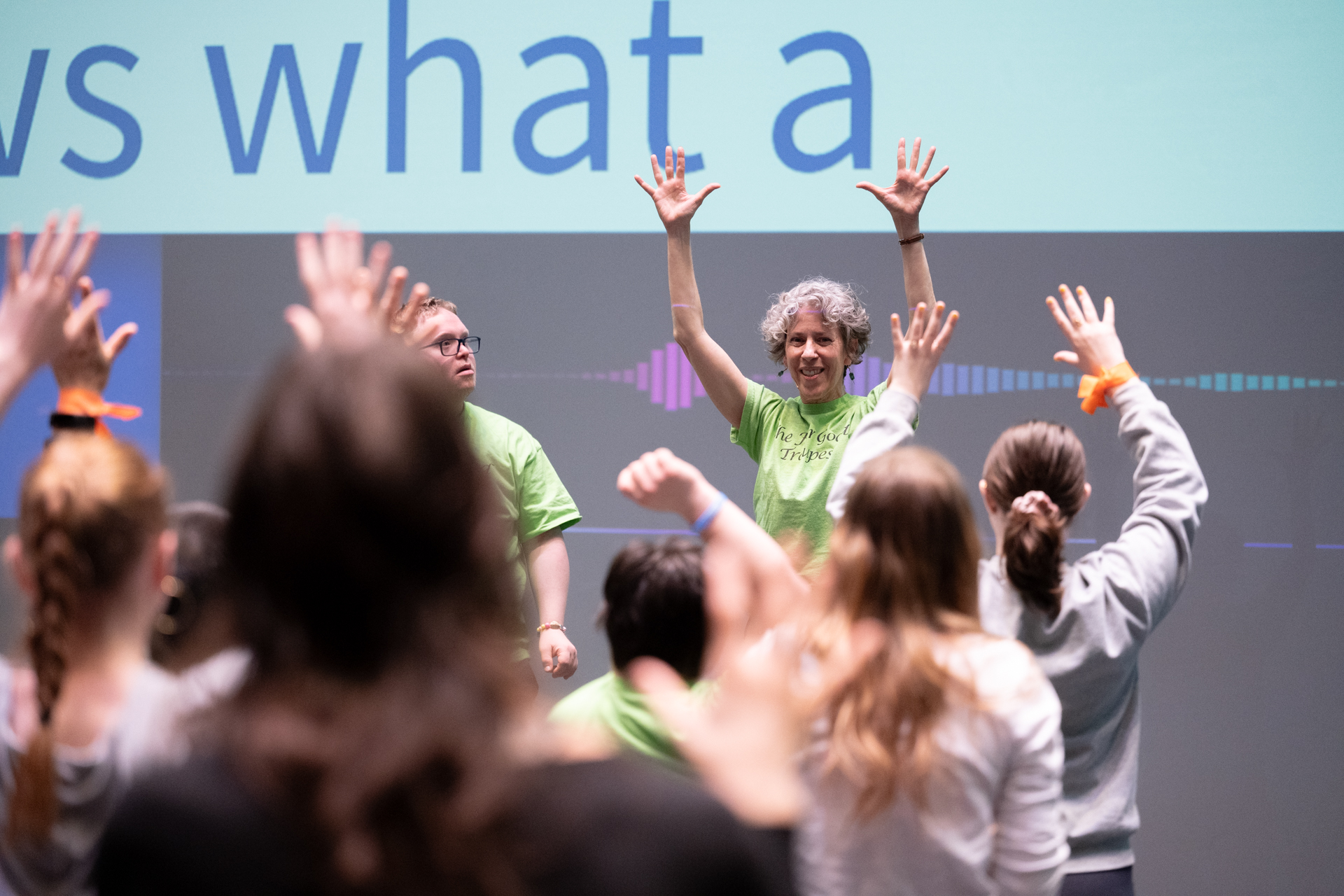 A woman instructor raises her hands high in front of a group of dancers.