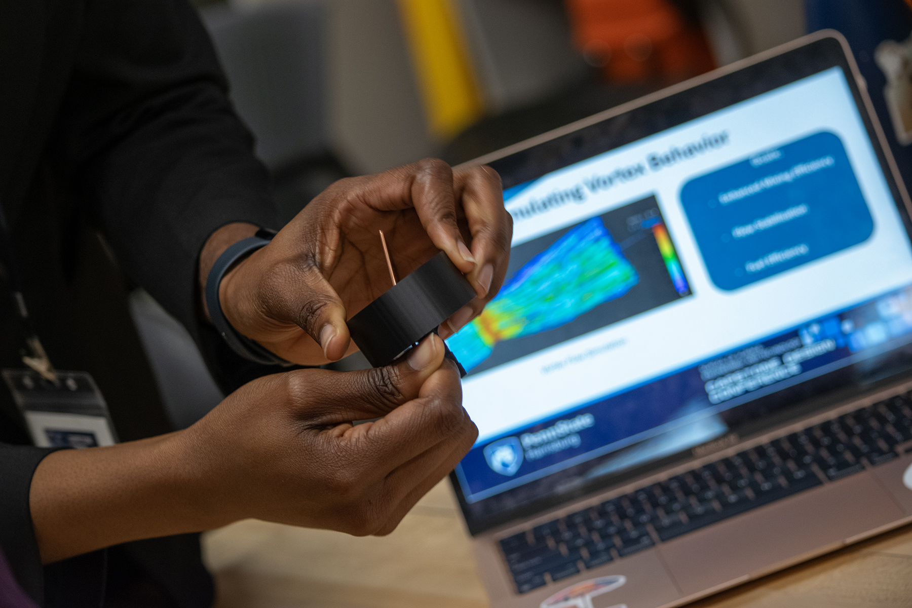 Closeup of a person's hands holding pieces of a science project, with a laptop in the background