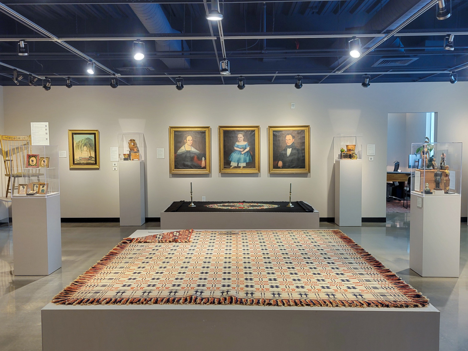 A gallery with classical paintings on the wall and textiles laid out for display throughout the room
