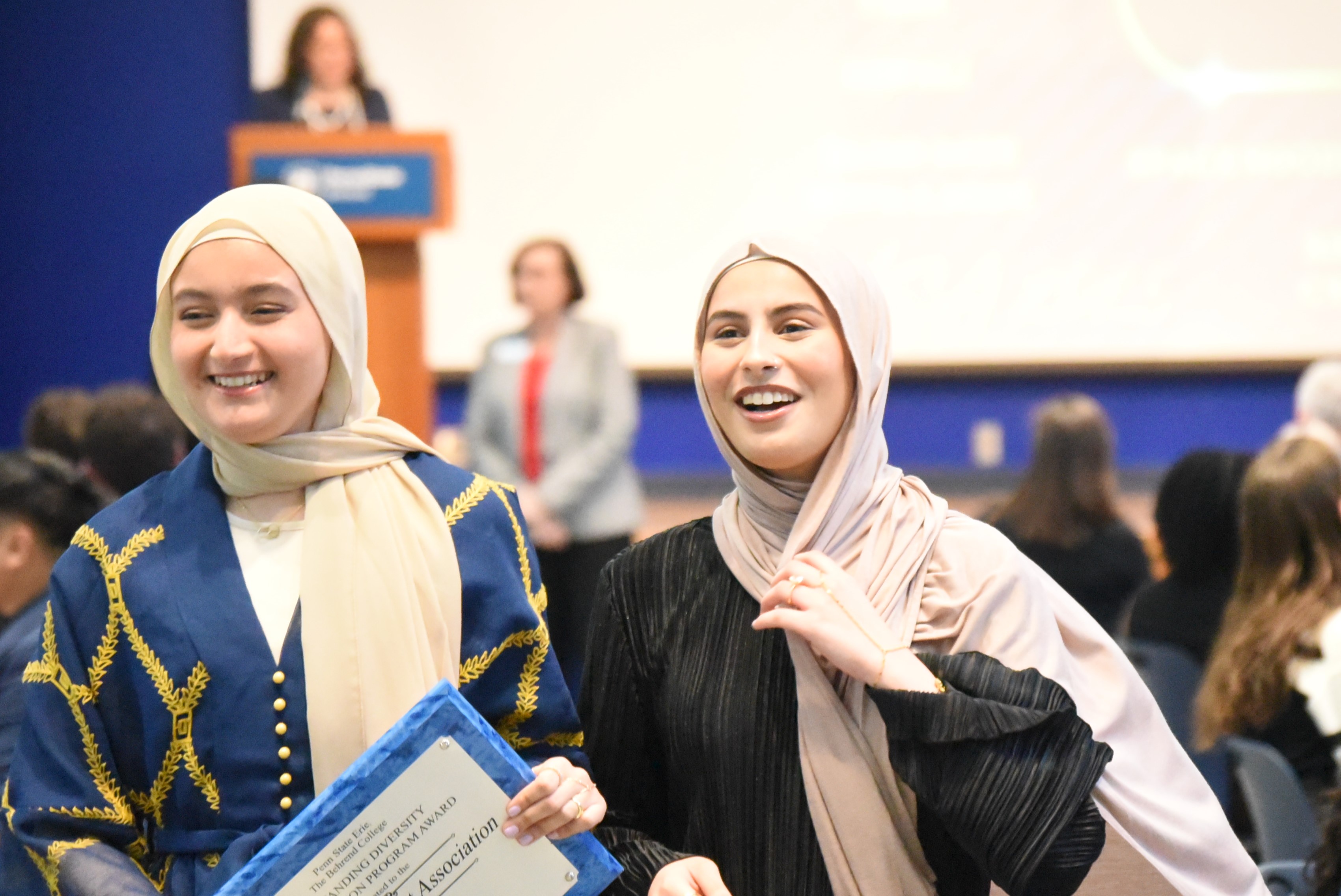 Two women in headscarves carry an award plaque at the Penn State Behrend Excellence in Leadership and Service Awards