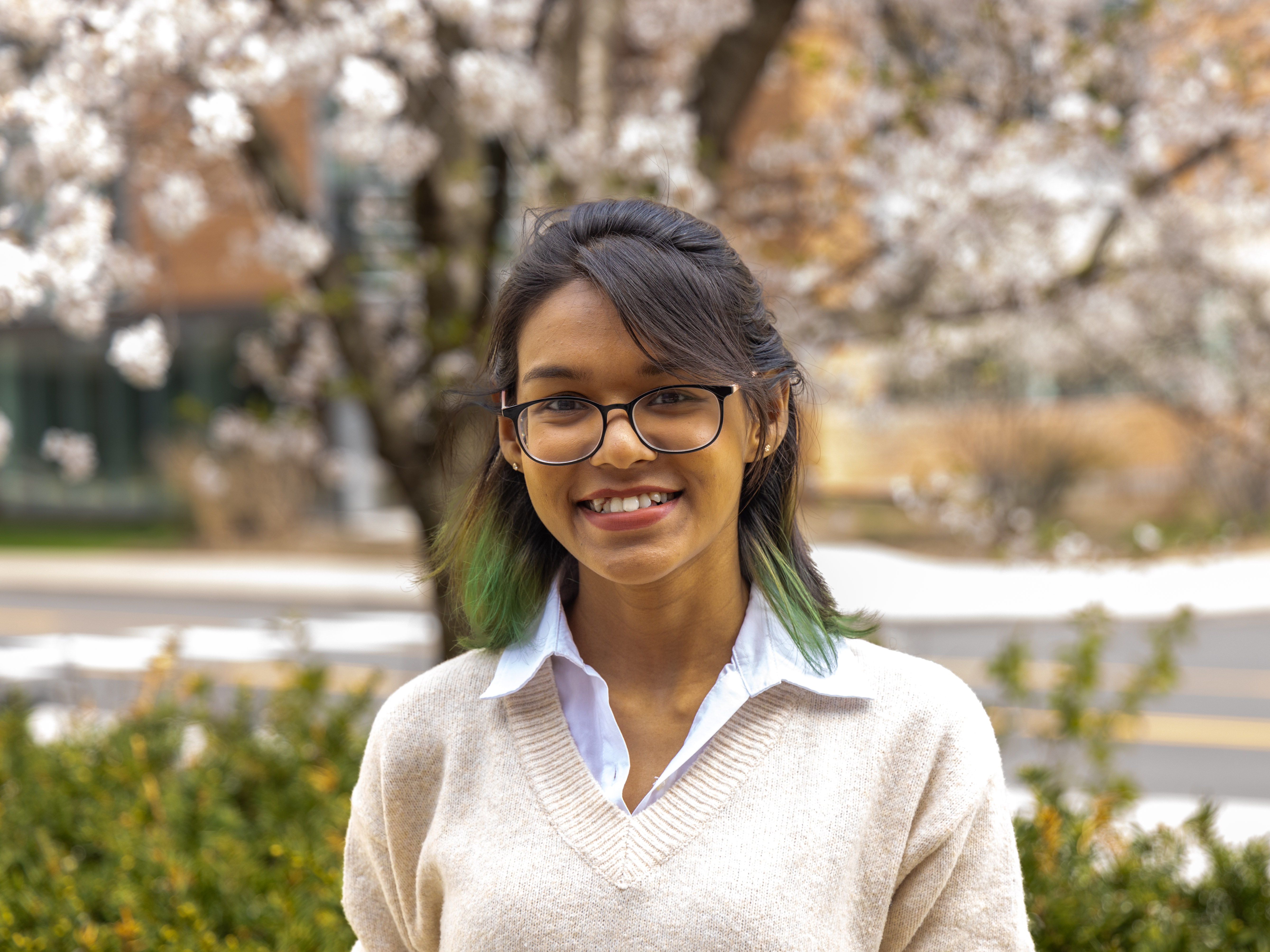Halima Binte Islam stands in front of a flowering tree and bushes at Penn State University Park.