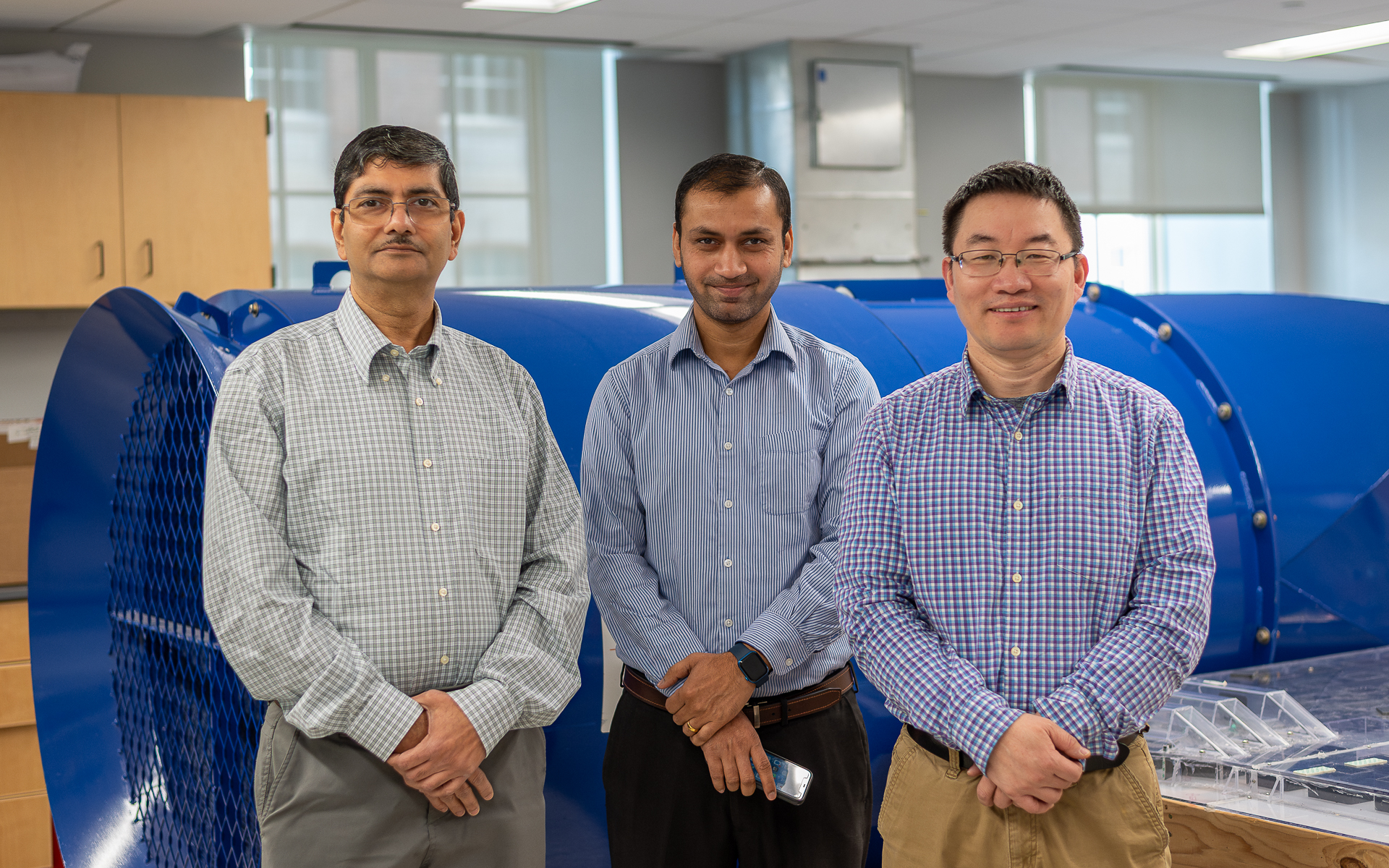 Sekhar Bhattacharyya, Ashish Kumar and Shimin Liu standing in front of a large blue fan in the mine ventilation lab.