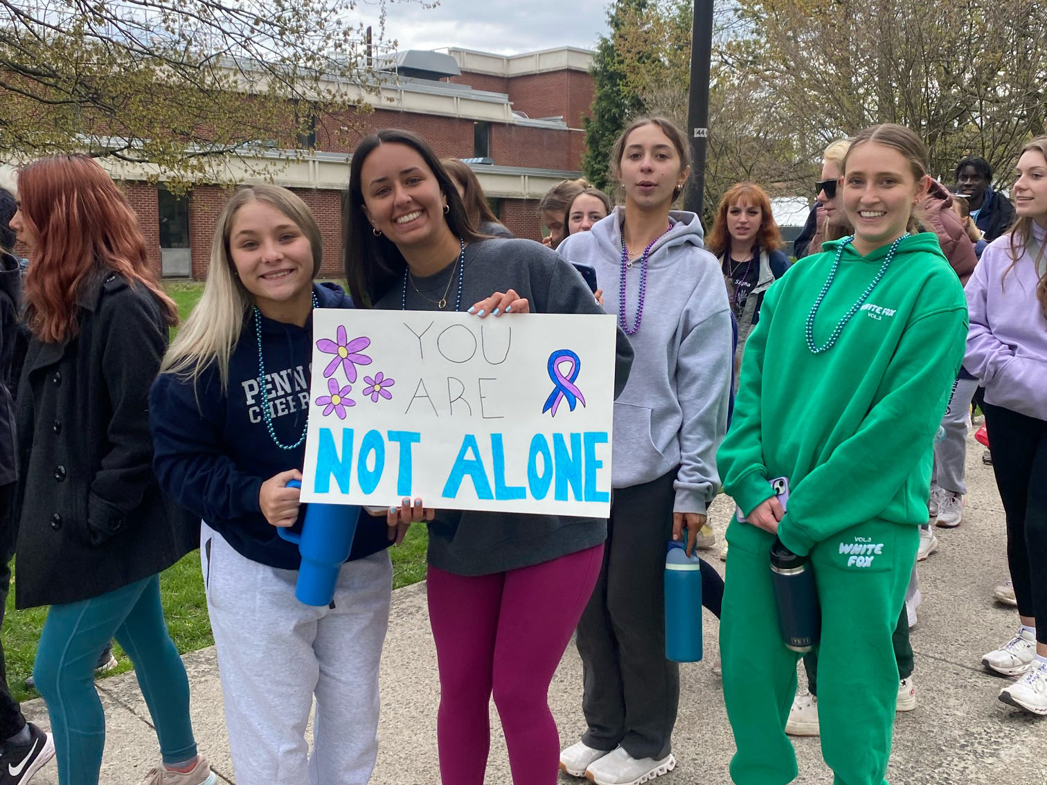A group of students hold up a sign that says You Are Not Alone