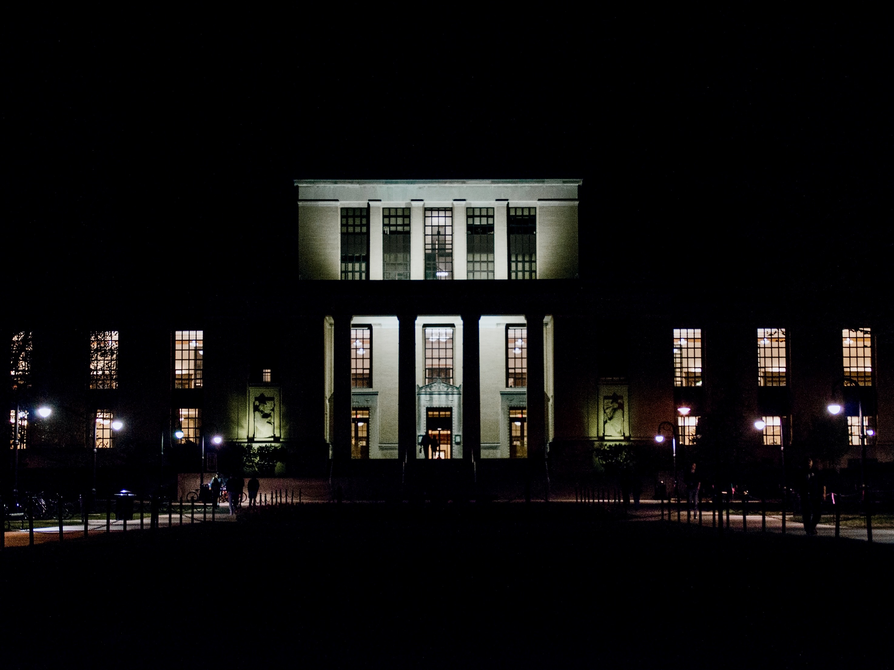 large building entrance with stairs, tall pillars lit at night