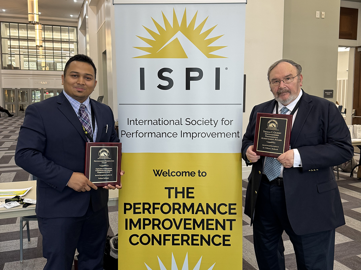 Farhan Sadique and William Rothwell posing near banner with awards.