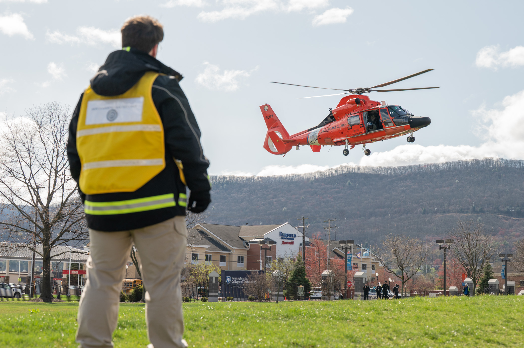 A person watches a red helicopter landing on a lawn