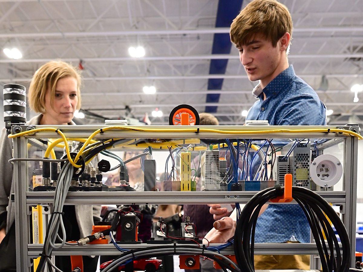 Dr. Megan Nagel, regional chancellor, listens as a student explains his engineering project at Penn State New Kensington’s annual Research and Student Engagement Expo. Cables and equipment are visible in the foreground as part of the student’s display.