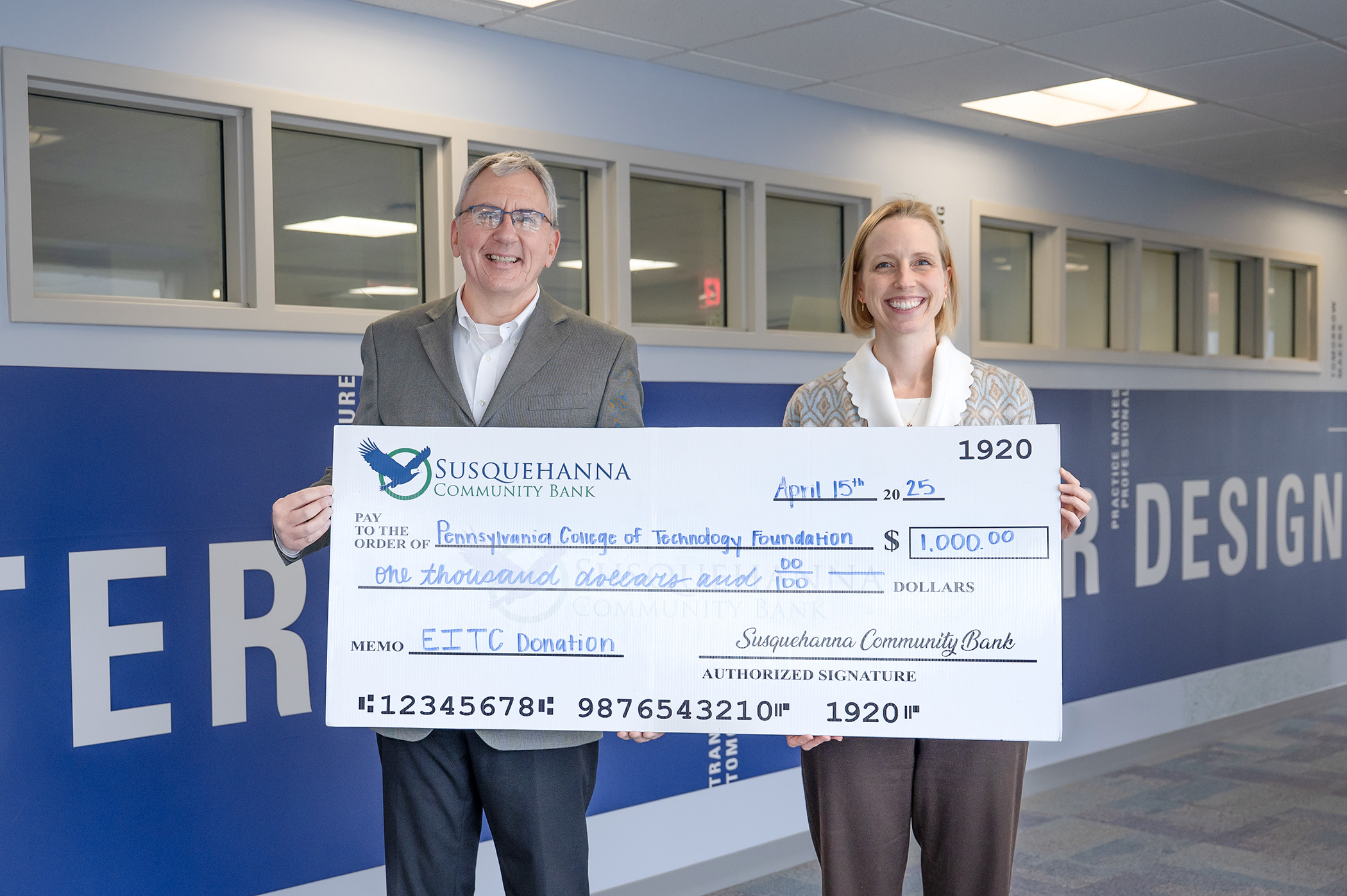 Two smiling people hold up a big check