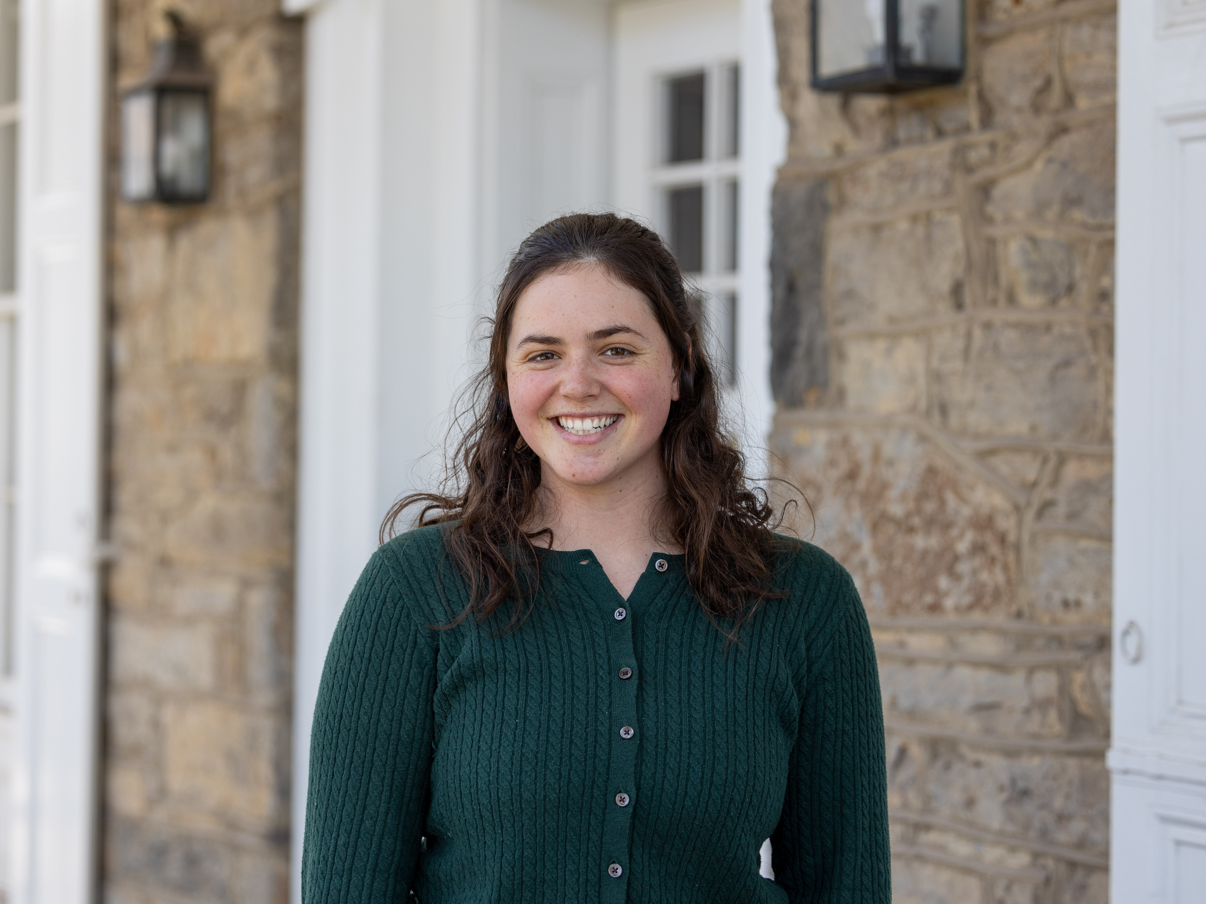 Lucy Taylor stands outside the University House wearing a green button-down sweater.