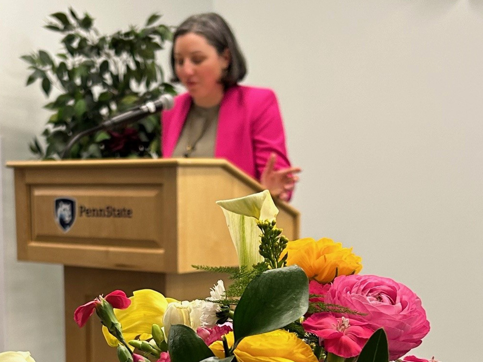 Woman speaking at podium with flowers in foreground