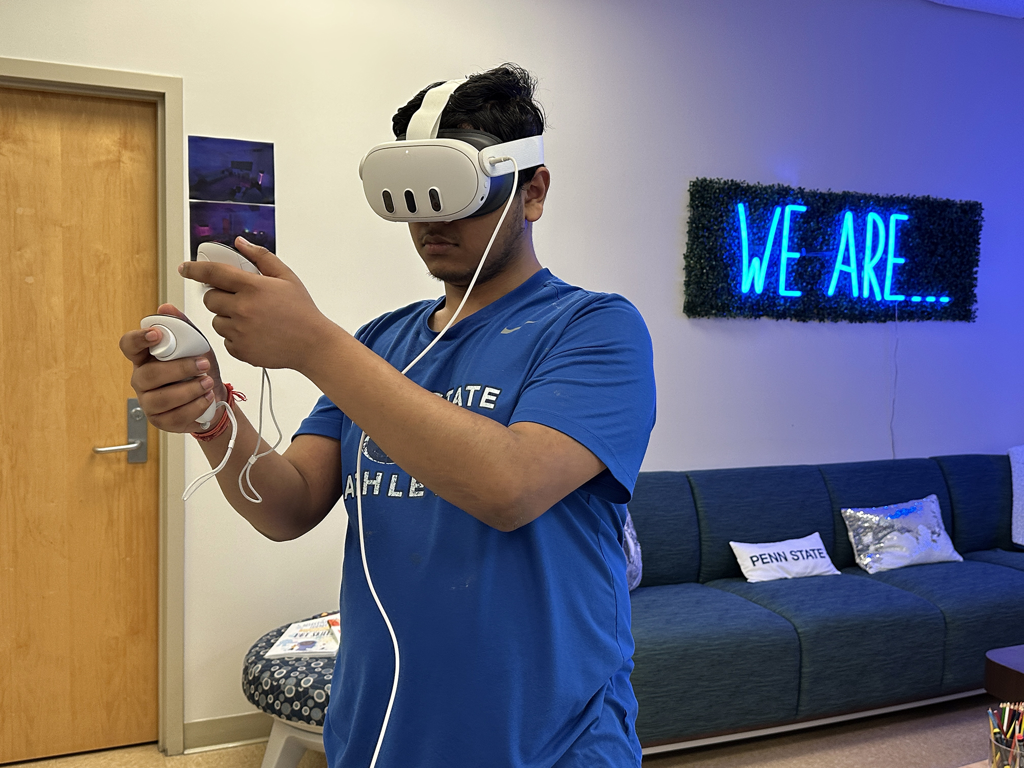 A student wearing a blue t-shirt tries a VR headset. He stands and reaches his arms forward.