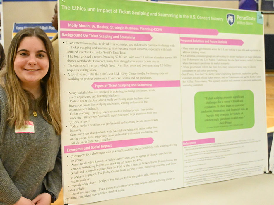 A woman stands at left next to a large research poster on a table.