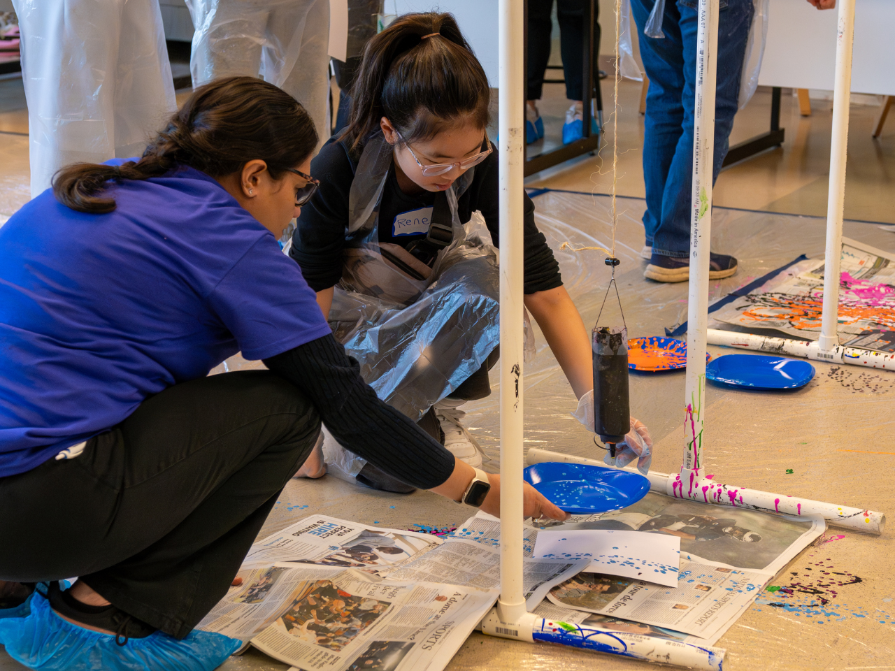 Two people crouch down to examine a science experiment on the floor
