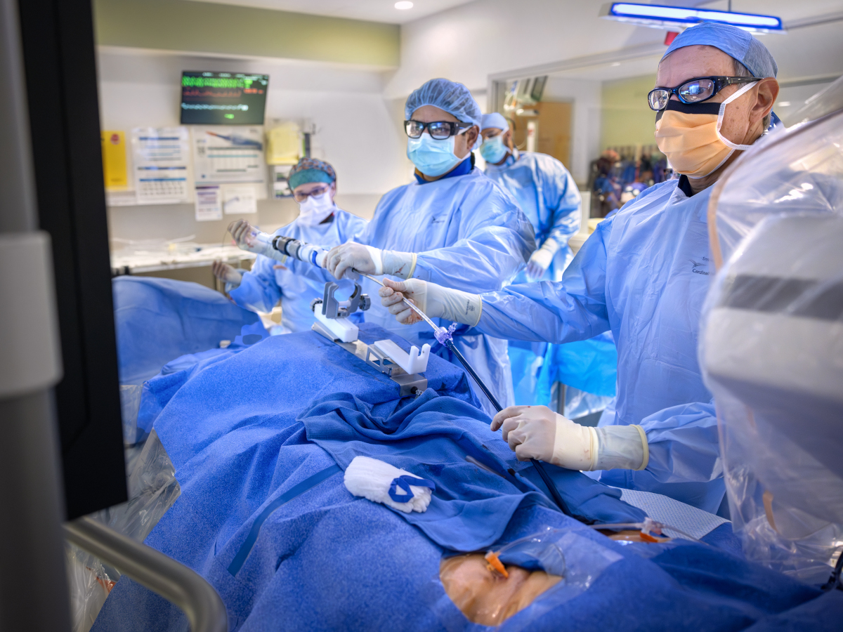 A team of medical professionals in full surgical attire, including masks, gowns, and protective eyewear, performs a minimally invasive procedure in a hospital operating room.