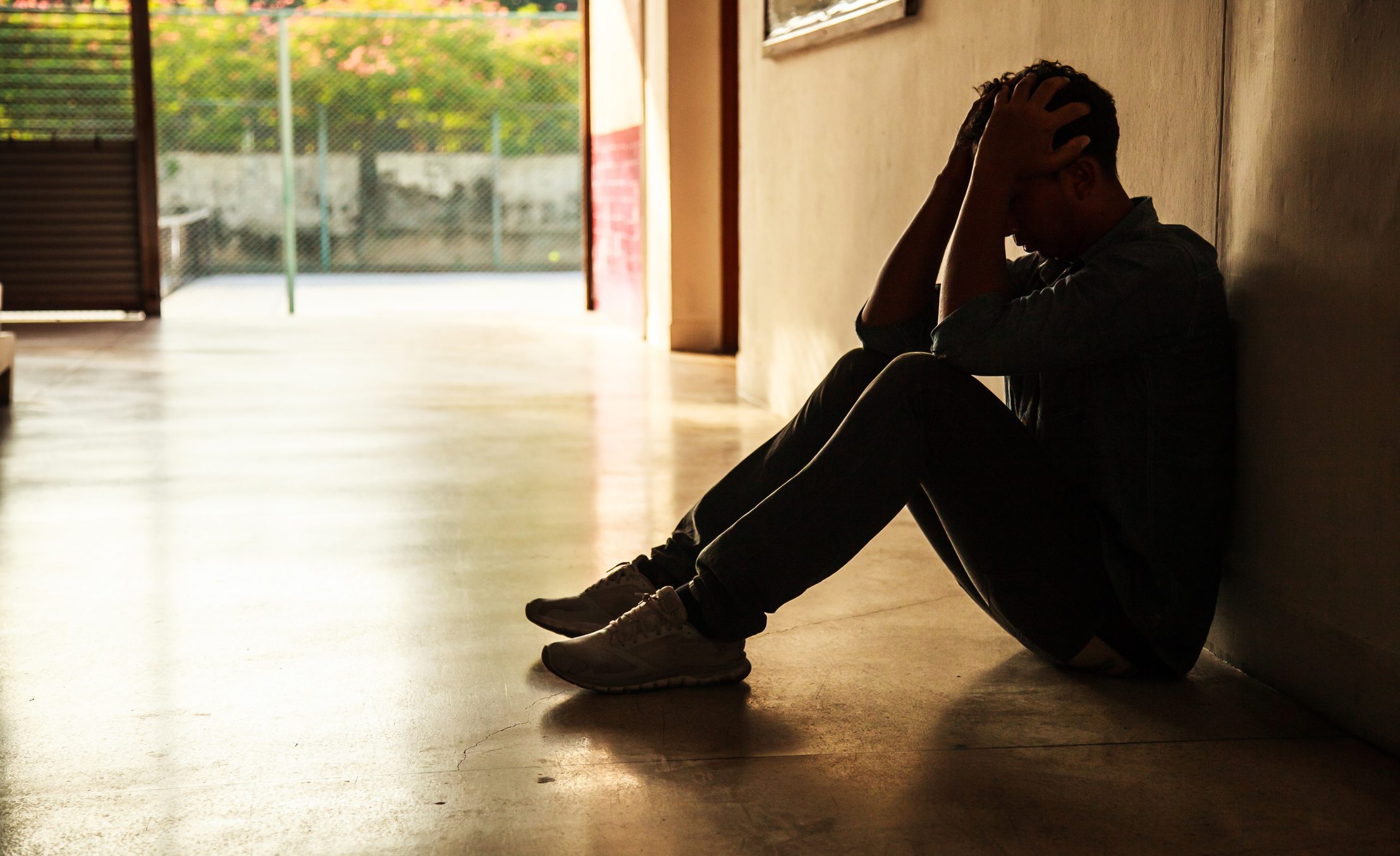Person sitting on hallway floor holding head in hands.