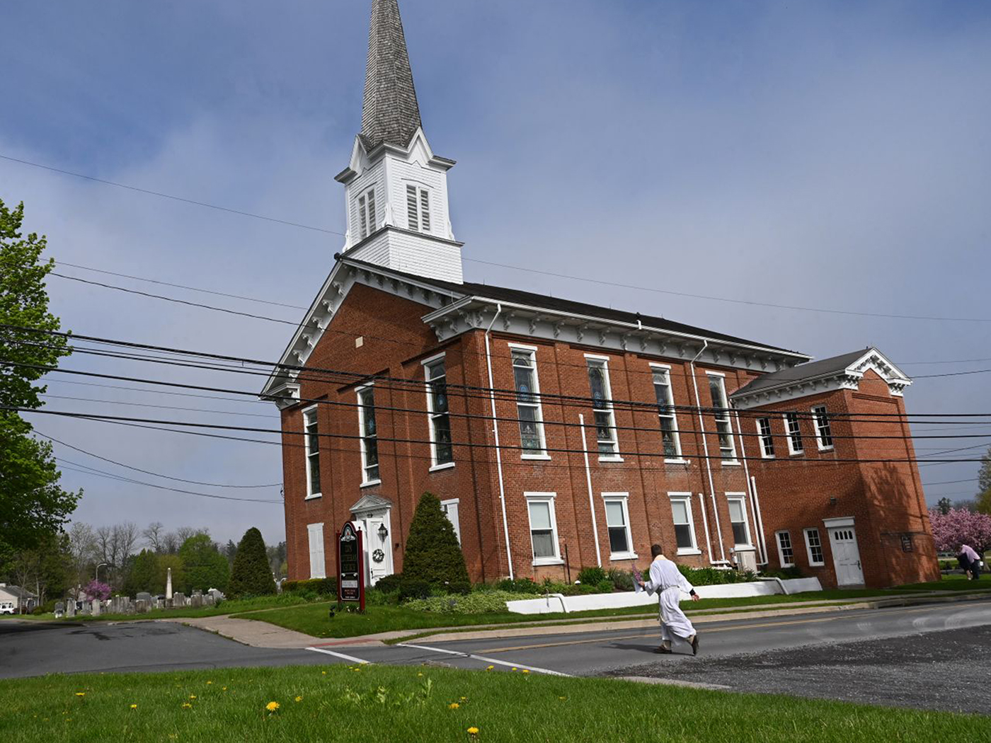 Man in white robe walks toward a red brick church