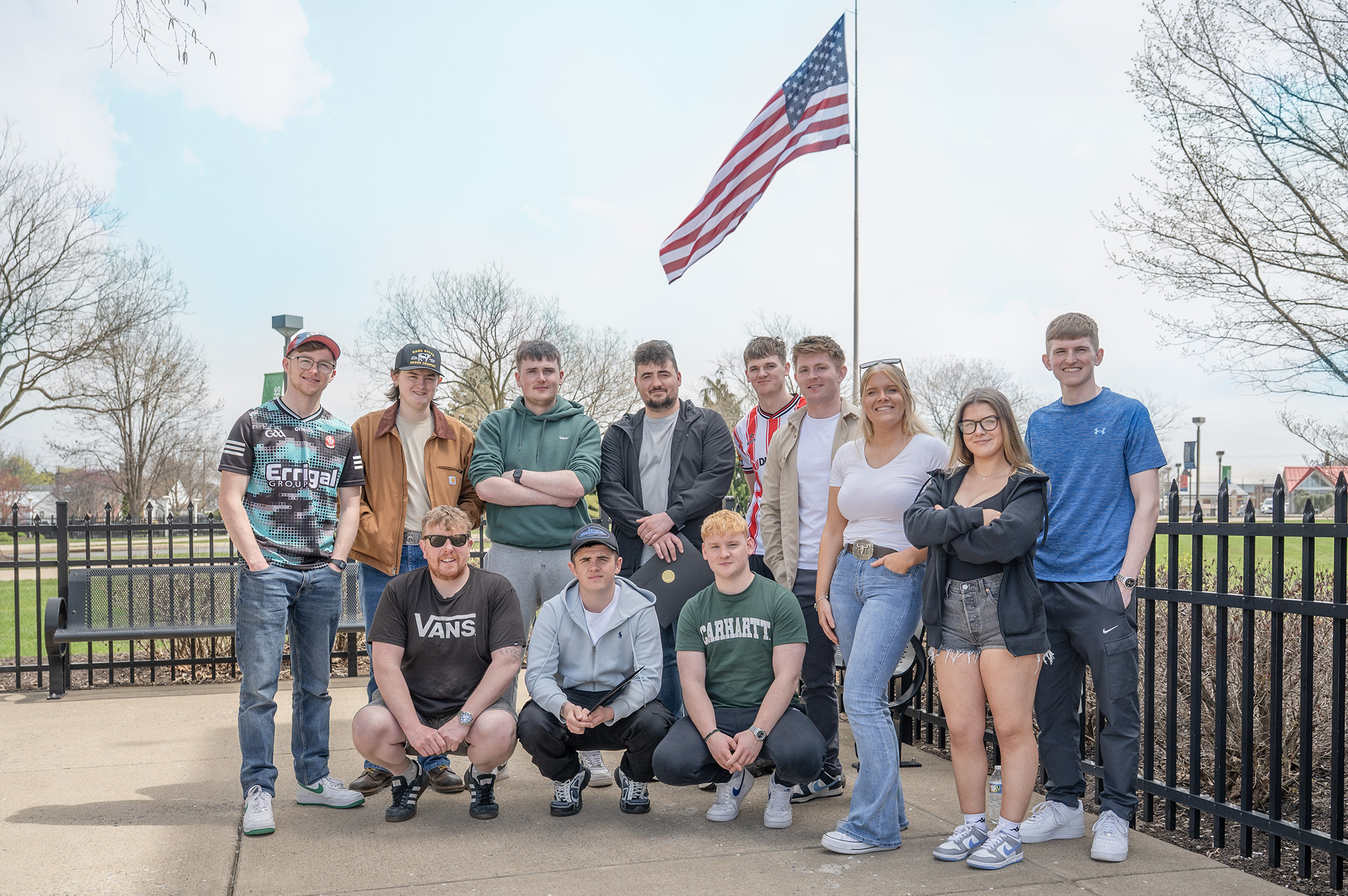 A group of students pose for a photo outside under an American Flag pole.