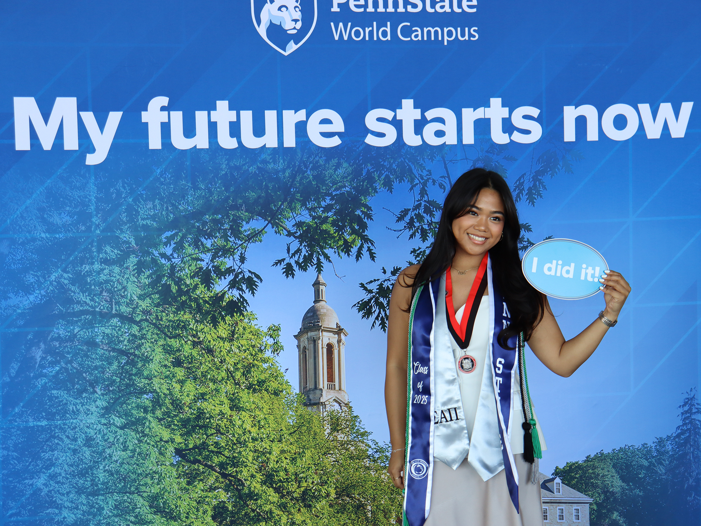 A woman wearing graduation stoles poses in front of a Penn State photo background.