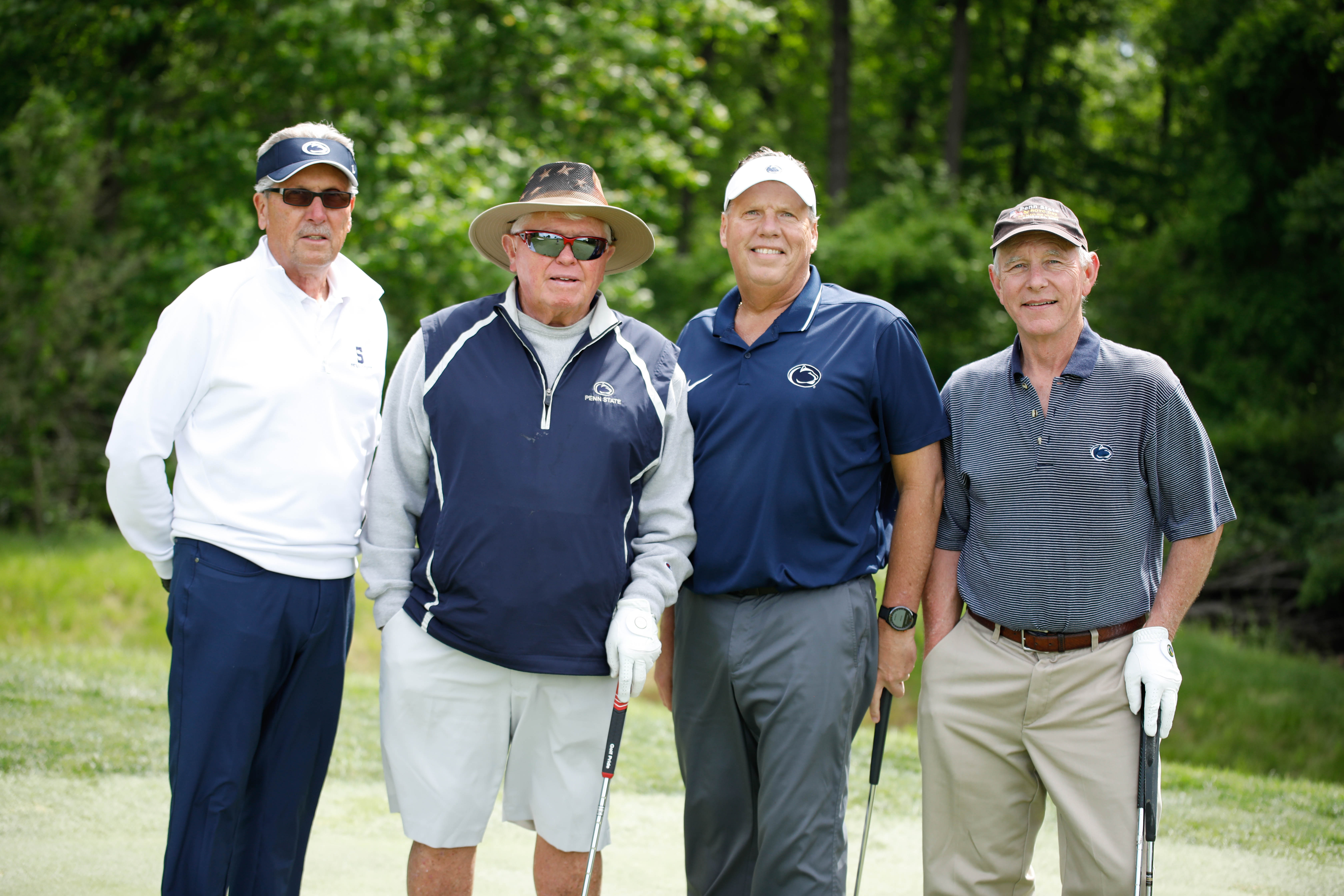 Four golfers stand on a course with their golf clubs. 