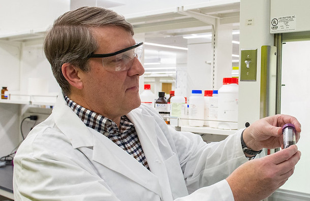 Man in lab coat looking at vial of bio-oil. 