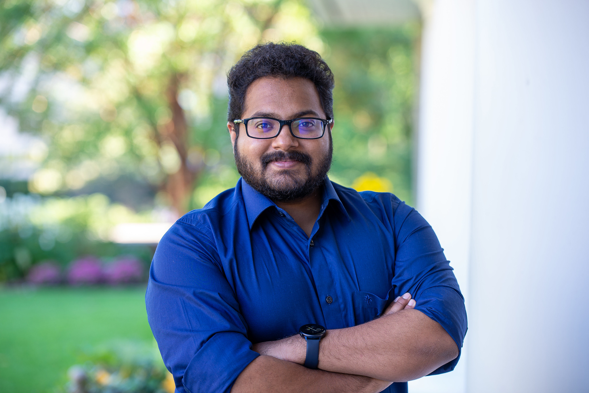 A faculty member wearing glasses and a blue buttoned shirt smiles for a picture