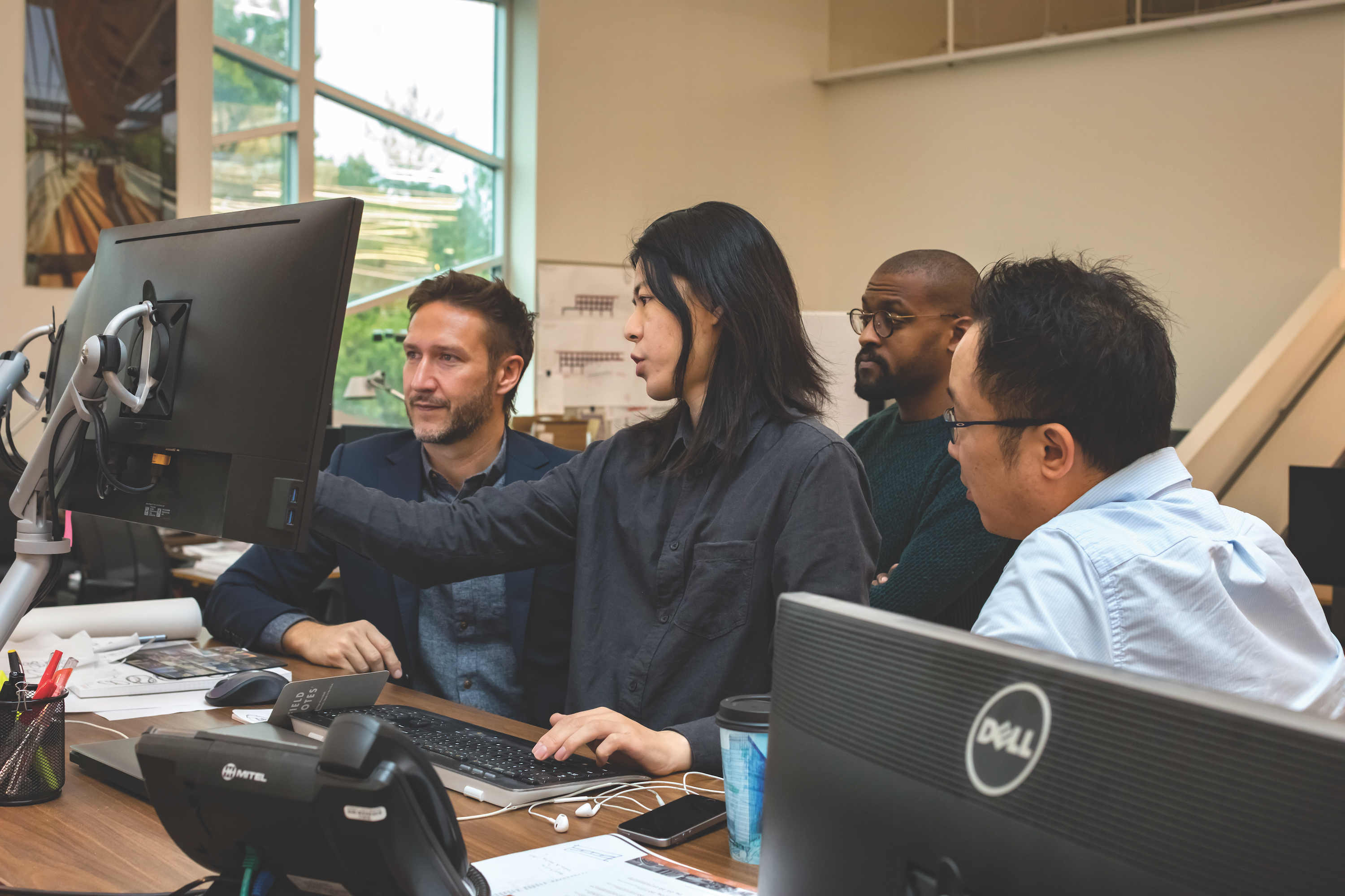 Four people sit around a monitor in a design office