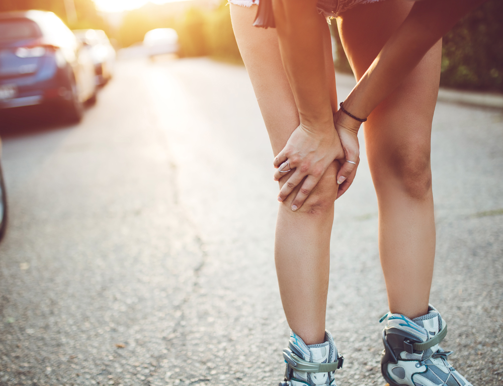 A close-up of a female runner’s legs. She grasps her right knee with both hands, as if in pain.