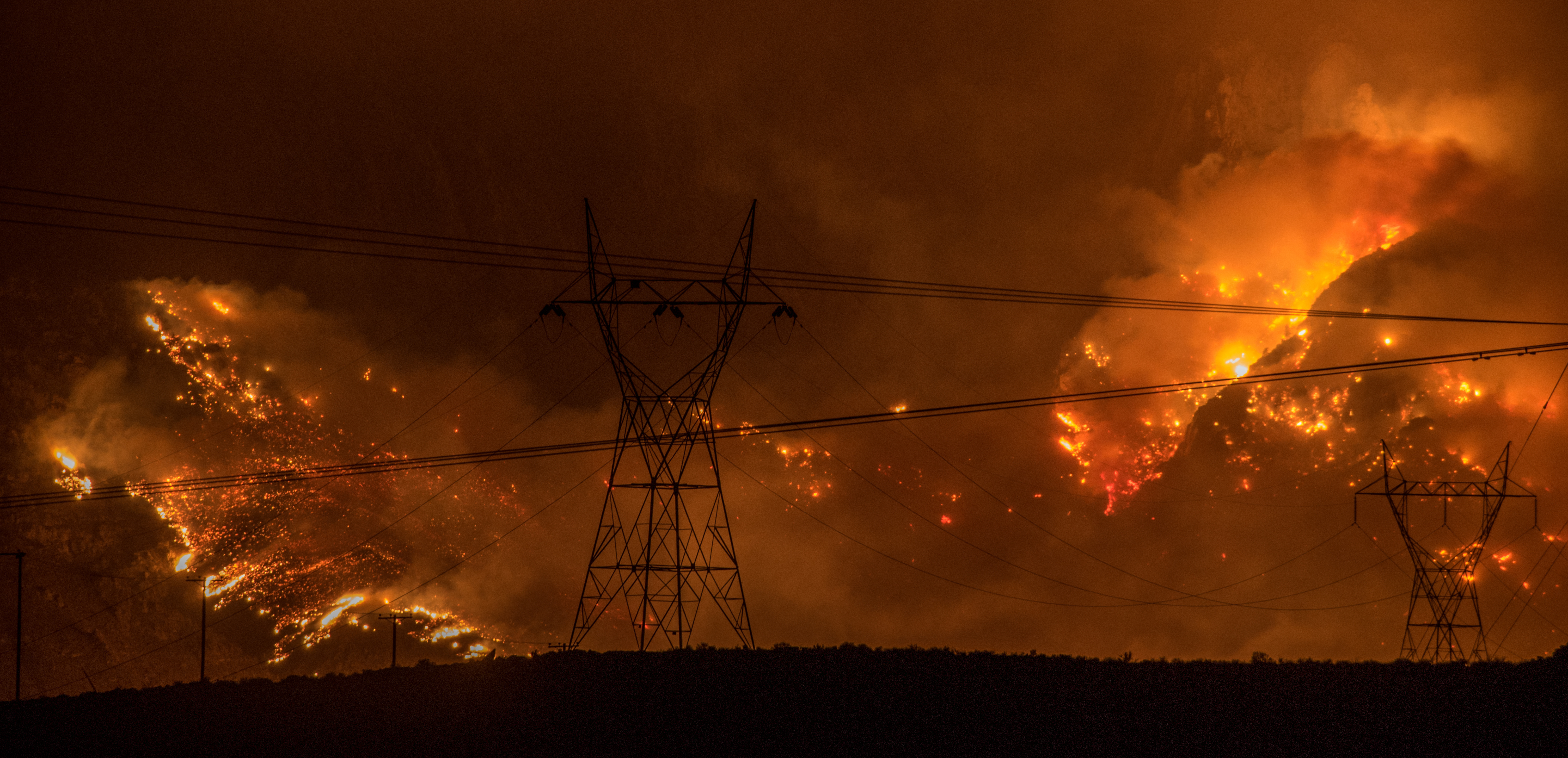 Wildfires in California burn behind transmission lines. 