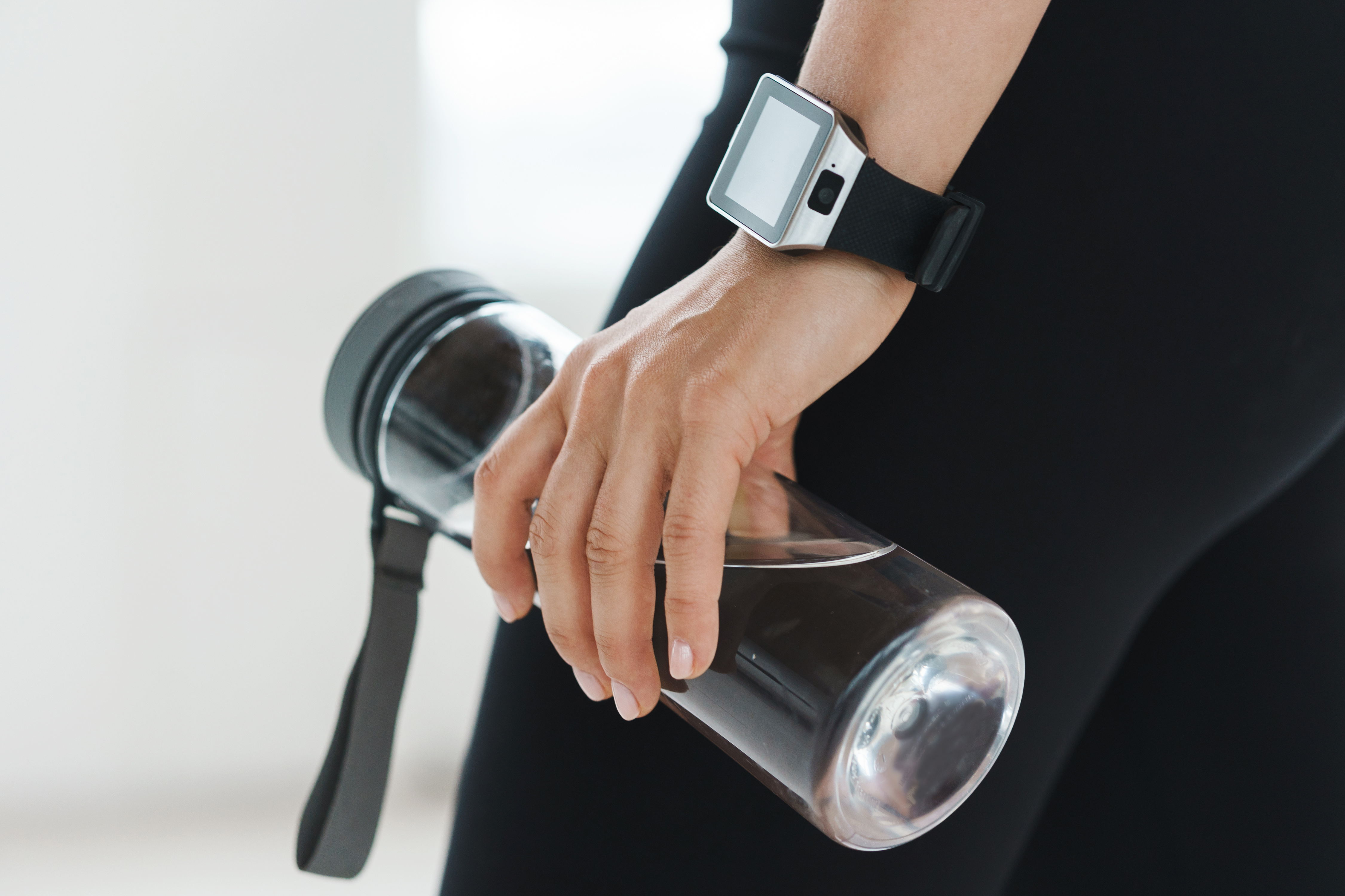 A hand wearing a Smartwatch and holding a water bottle