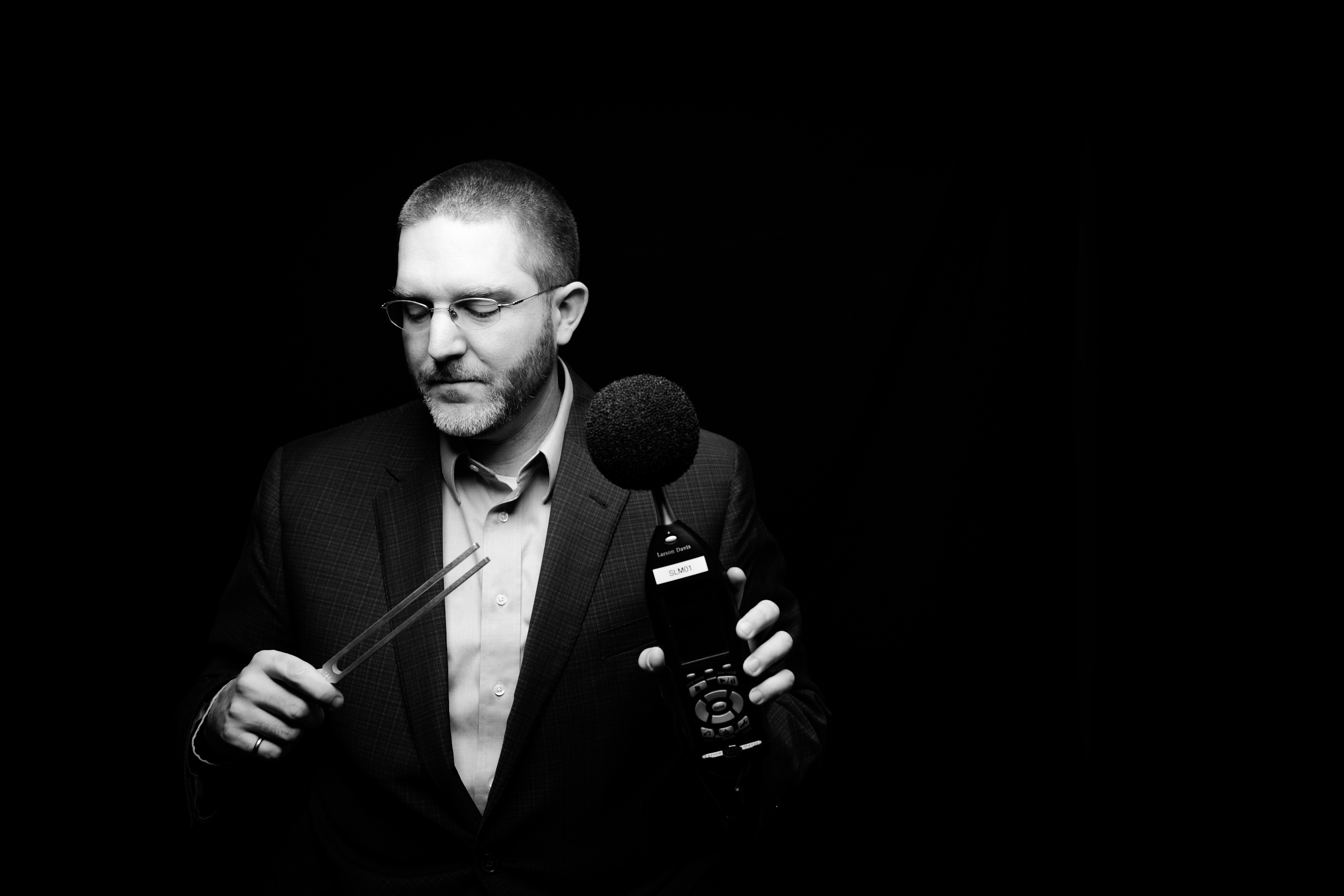 black and white photo of a professor posing with acoustics equipment (tuning fork and microphone)