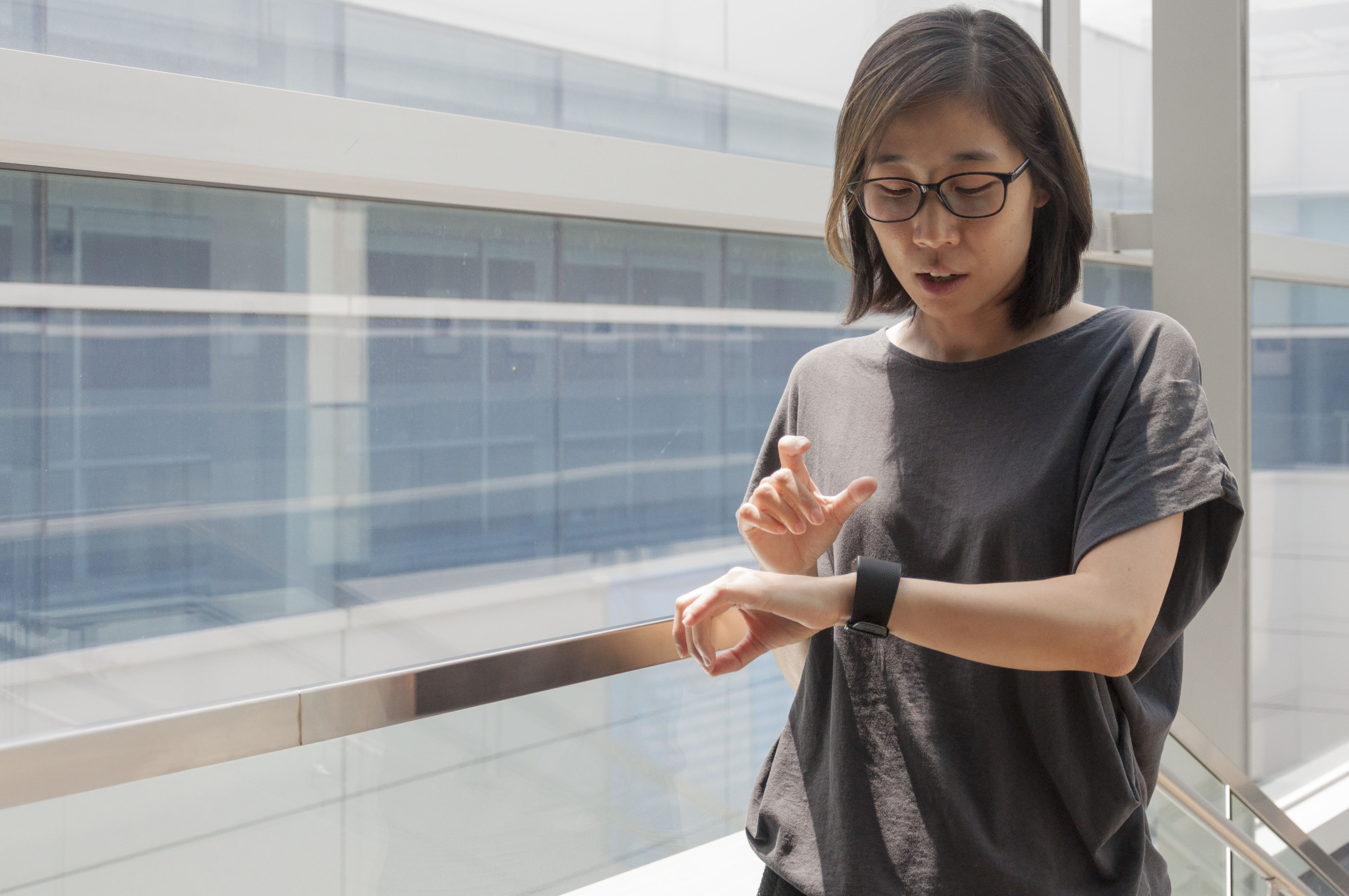 A woman in a gray top looks at the FitBit monitor on her wrist