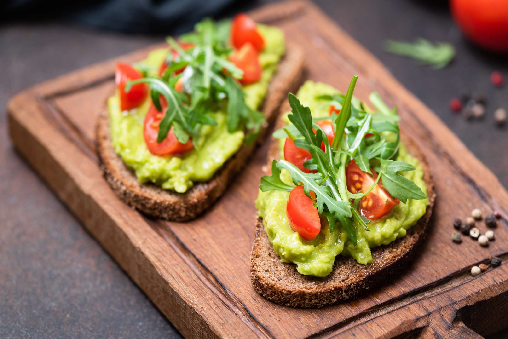 A cutting board with two pieces of avocado toast on it