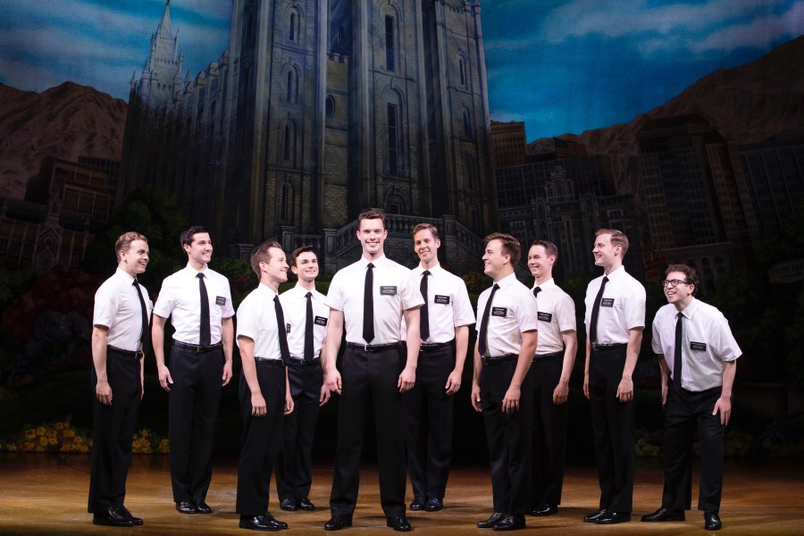 A group of men wearing matching button-down shirts and slacks smile while they stand in a row.