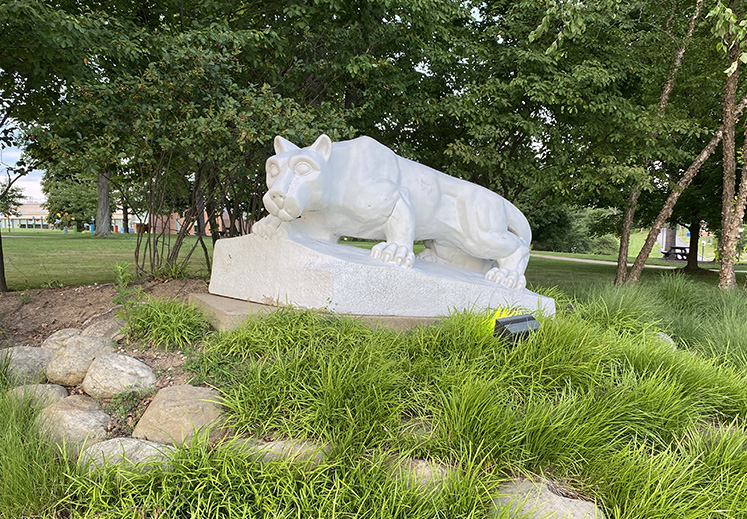 The Nittany Lion shrine sits among greenery in front of the campus quad