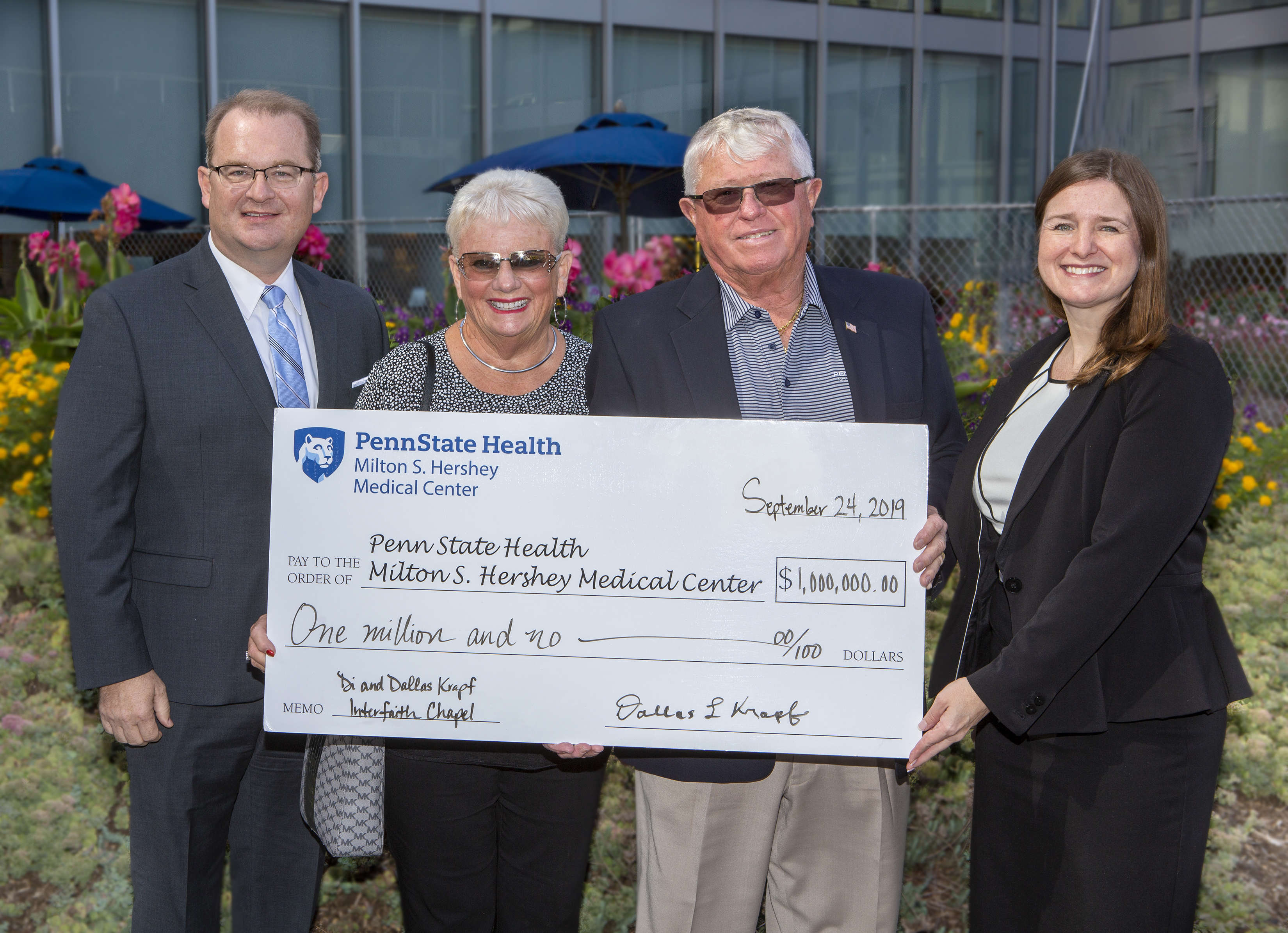 Four people – two men and two women – pose outside for a photo holding an oversized check made out to Penn State Health Milton S. Hershey Medical Center, in the amount of $1 million. It’s signed by Dallas Krapf. 
