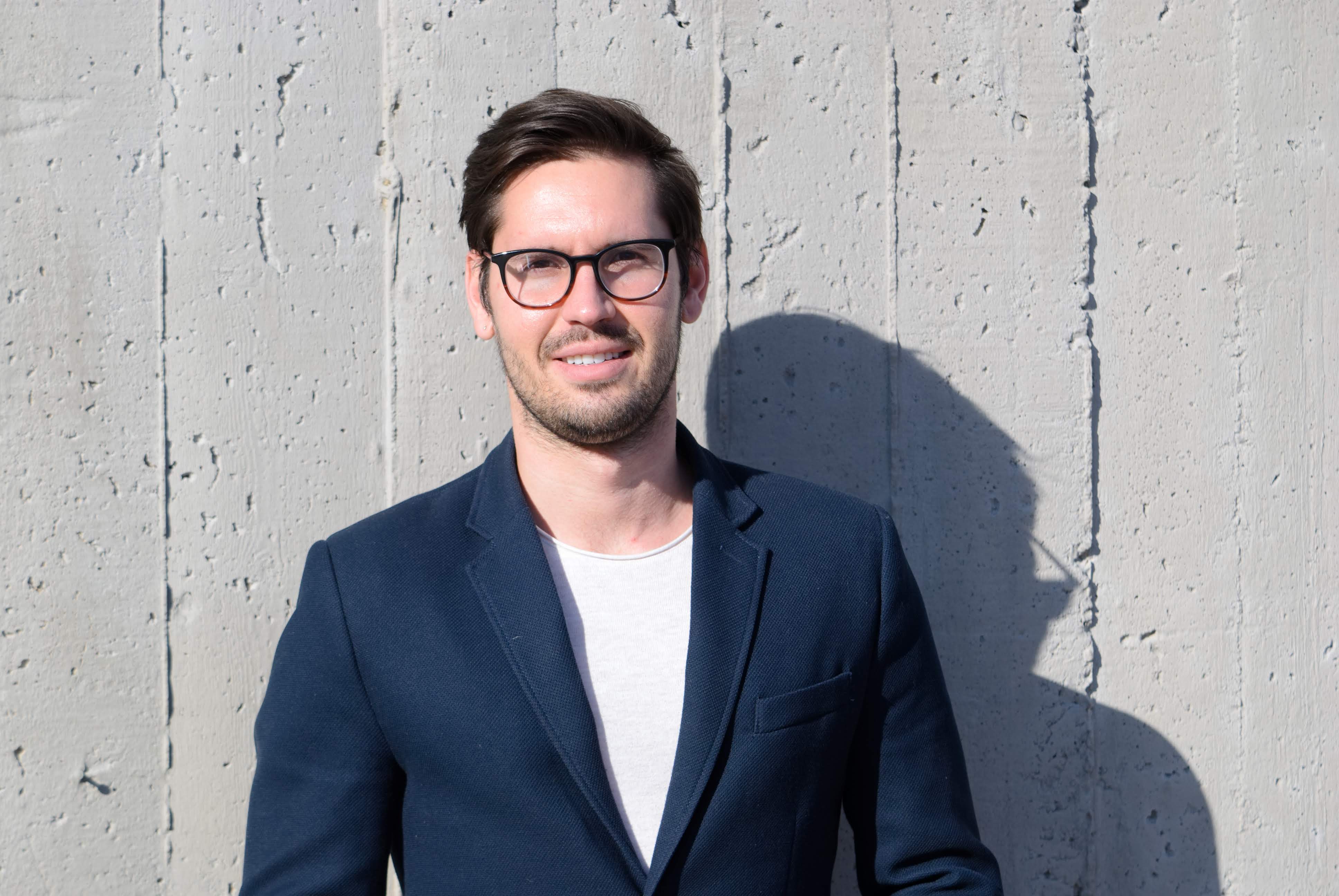 casual photo of head, shoulders and chest of fair-skinned, dark haired, younger man with dark-rimmed glasses.