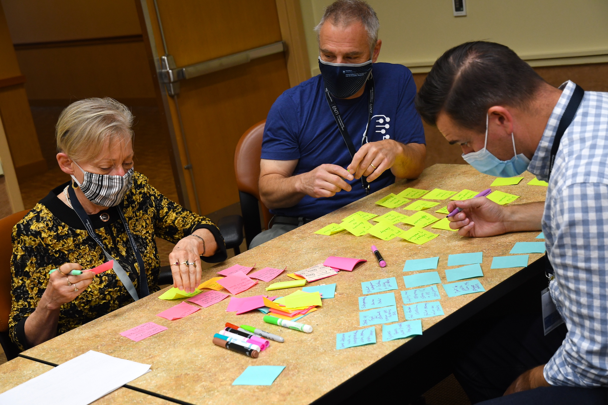 Three people around a table writing on sticky notes