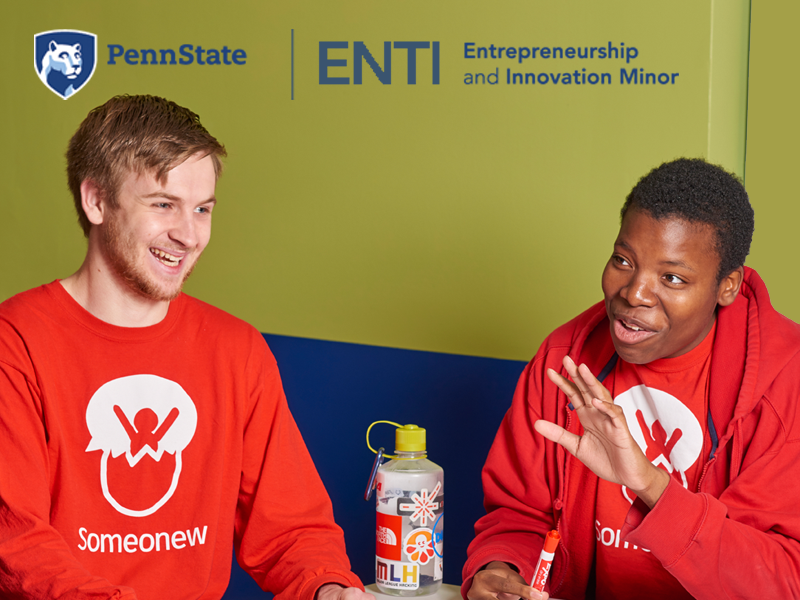 Two students, the creators of the Someonew app, sit together smiling, discussing entrepreneurship wearing red Someonew teeshirts