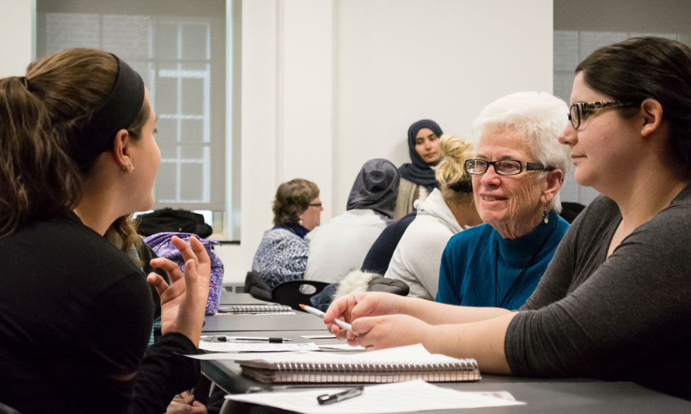 Two female students interact with an older female student.