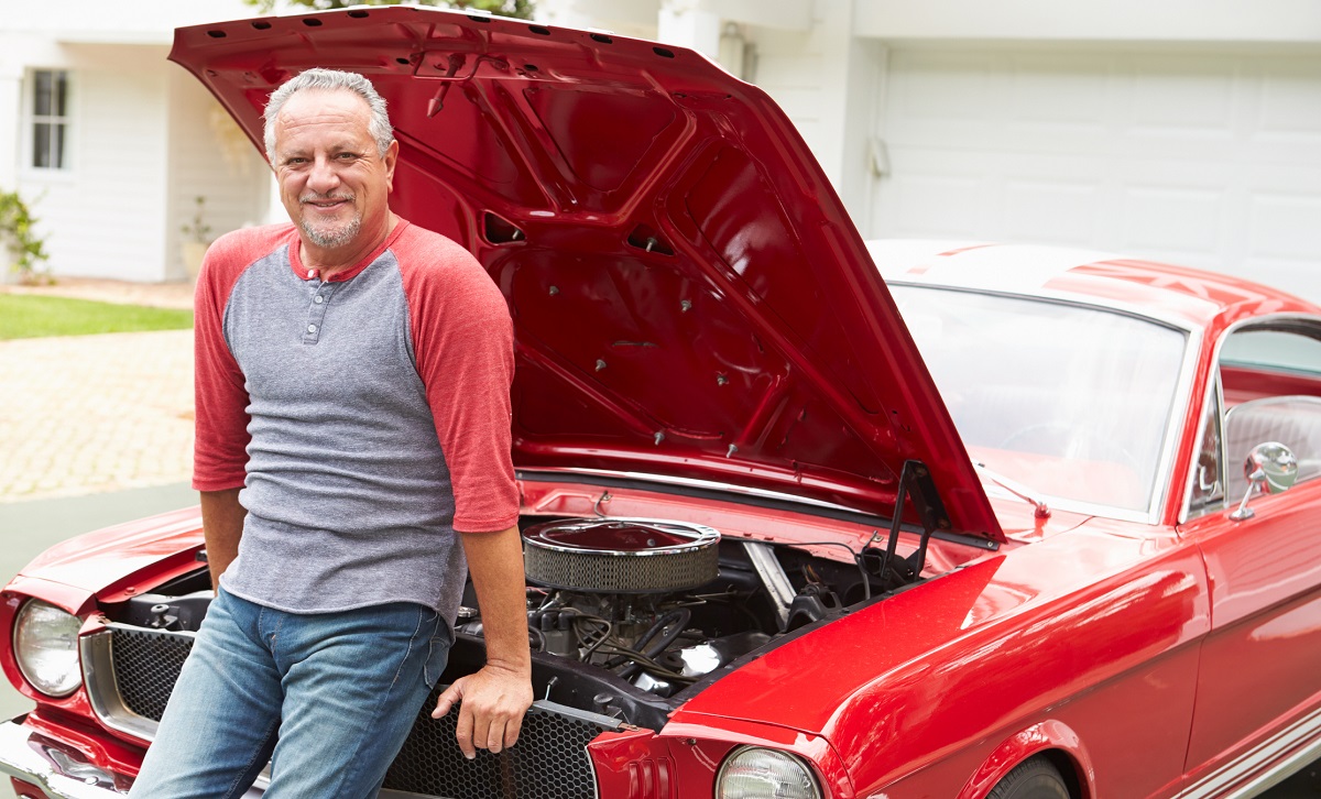 Retired senior man sitting on front of restored classic car.